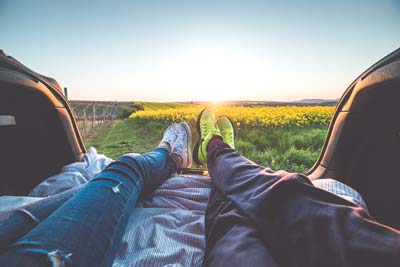 A couple lounging behind a car, watching the sunset